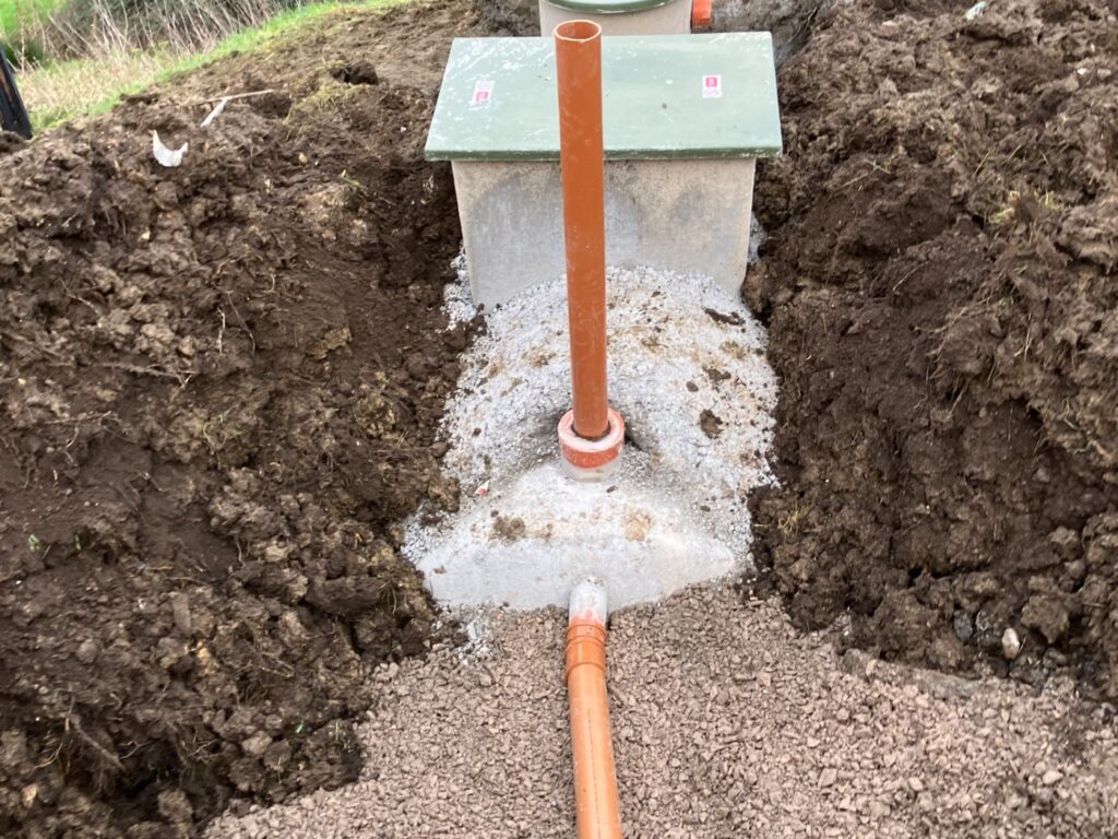 Orange discharge pipework running from a septic tank chamber along an open trench