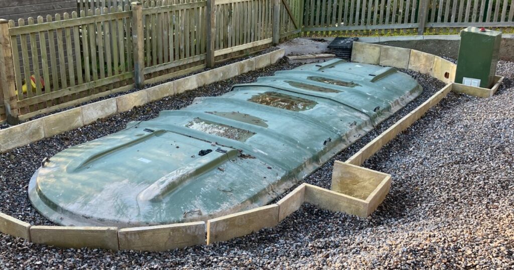 A small sewage treatment plant bedded on shingle in a garden, backfill under way