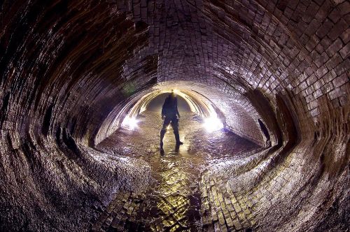 Man stood inside a large underground sewer tunnel as an example of confined space drainage access